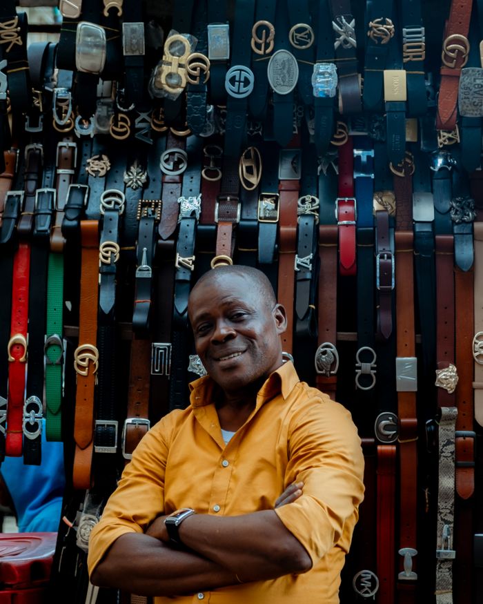 The Art of Drawing Readers In: Your attractive post title goes here Smiling vendor showcasing diverse belt collection in Lagos market.