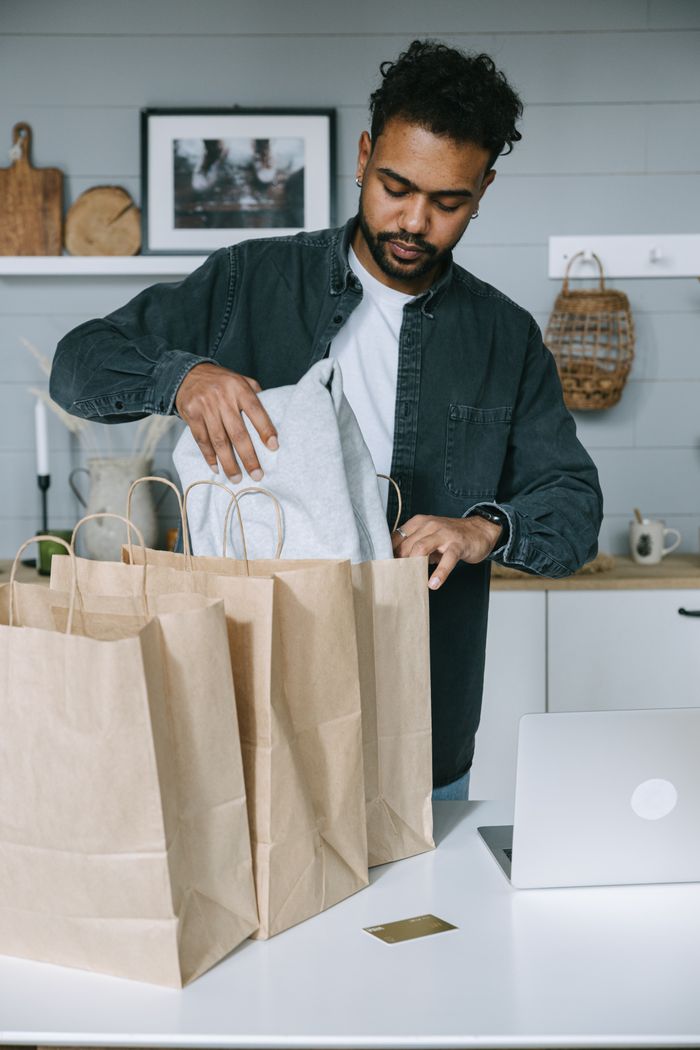 services-05 Adult man organizing purchases with paper bags and laptop in a modern home setting.